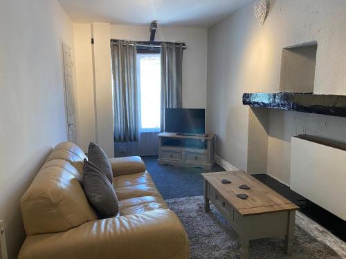 a living room with a leather couch and a tv at Rosecraddoc Manor - Coachman's in Saint Cleer
