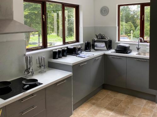a kitchen with grey cabinets and a sink and windows at Rosecraddoc Manor - Riverbank in Saint Cleer