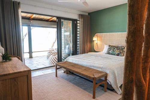 a bedroom with a bed with a bench and a balcony at La Pépite Villa in Pointe d'Esny