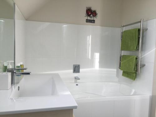 a white bathroom with a white tub and a green towel at Davidsons Luxury Homestay in Lower Hutt