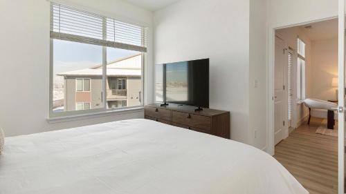 a white bedroom with a large bed and a television at Landing Modern 2BD Gym Clubhouse in Longmont