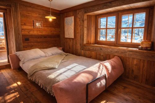 a bed in a room with wooden walls and windows at Casalpina Cozy chalet in Gressoney-la-Trinité
