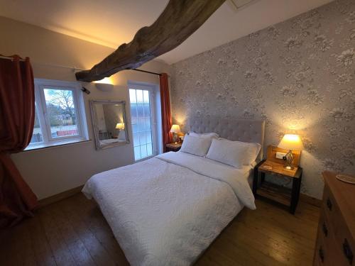 a bedroom with a white bed and two windows at The Mews @ The Pheasant in Ironbridge