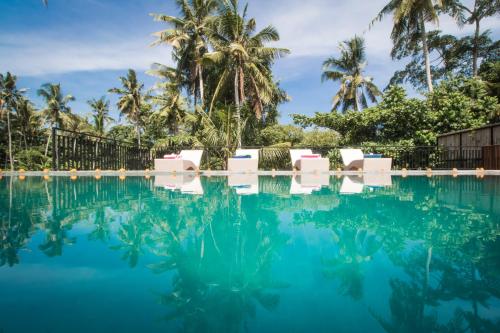 a swimming pool with white chairs and palm trees at Junjungan Serenity Villas & Spa in Ubud