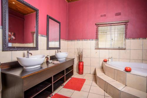 Baño con 2 lavabos, bañera y paredes rosas en Abangane Guest Lodge, en Hazyview