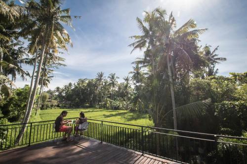 a man and woman sitting at a table on a wooden deck at Junjungan Serenity Villas & Spa in Ubud