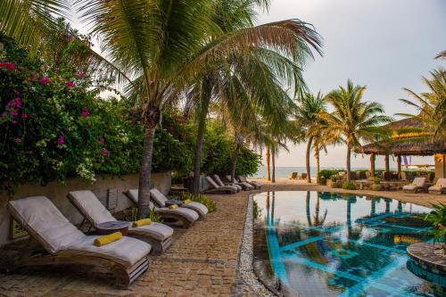 - une piscine avec des chaises longues et des palmiers dans l'établissement Sailing Club Resort Mui Ne, à Mui Ne