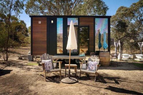 a small cabin with a table and chairs and a umbrella at Womburra Vineyard Tiny Stay by Tiny Away in Redbank
