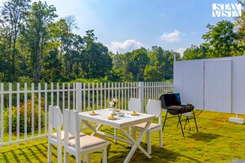 a white table and chairs on a patio with a fence at StayVista at Mudra Tattva - Pvt Pool,Lawn,Jacuzzi 2BR Luxury Rooms in Suntikoppa