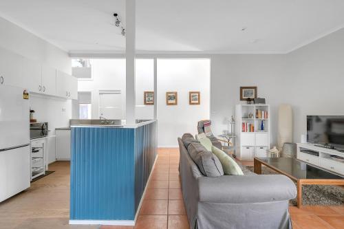 a living room with a couch and a kitchen at Cosy Getaway with Fireplace and Spacious Backyard in Broulee