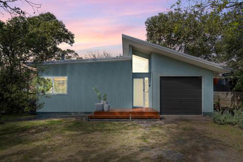 a blue house with a wooden porch in a yard at Cosy Getaway with Fireplace and Spacious Backyard in Broulee