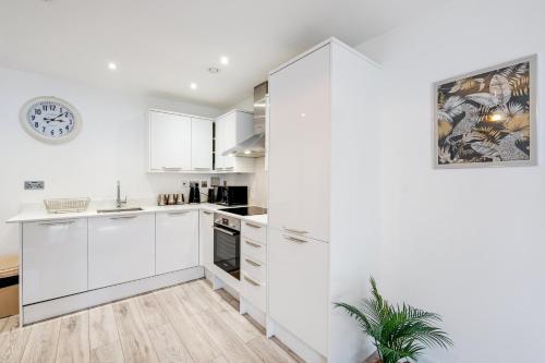 a kitchen with white cabinets and a clock on the wall at Multiple 2-Bedroom Apartments near Harry Potter Studios - 2-Minute walk to Bushey Station - 20 Minutes to London Euston - Ideal for Families & Business - Free Parking in Watford