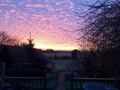 a sunset over a garden with a fence and a field at Fourwinds B&B in March