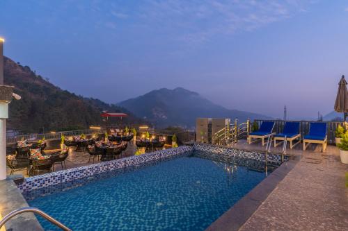 a resort pool with tables and chairs and mountains in the background at Perfectstayz Luxe kapilaz - Jacuzzi rooms in Bhowāli