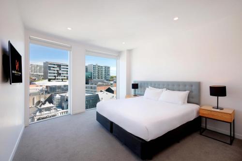 a bedroom with a white bed and a large window at Swiss-Belsuites Victoria Park Auckland in Auckland