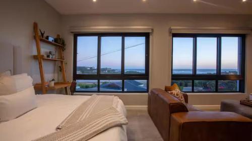 a bedroom with a bed and a couch and windows at Blue Bay Studio Apartment in Wilderness