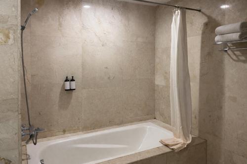 a bathroom with a bath tub with a shower curtain at Manna Hotel Pematangsiantar in Pematangsiantar