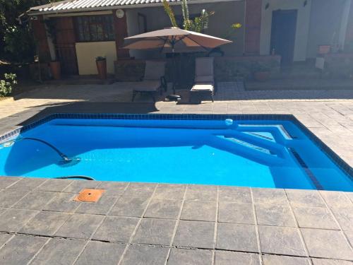a blue swimming pool with an umbrella and a chair at Lavender farm home in Port St. Johns