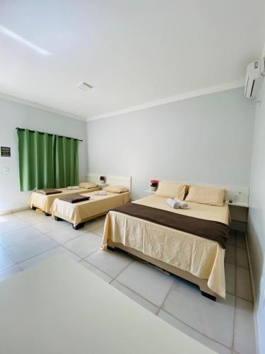 two beds in a room with green curtains at Hotel Pousada Marra in Catalão