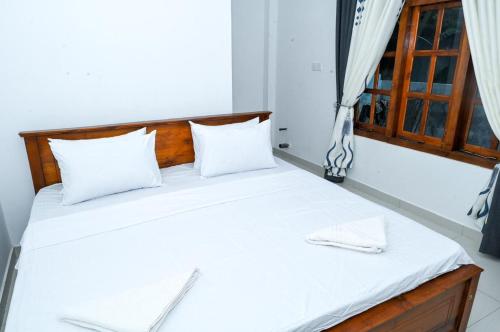 a bedroom with a bed with white sheets and a window at Rika Guest House in Kokkuvil East
