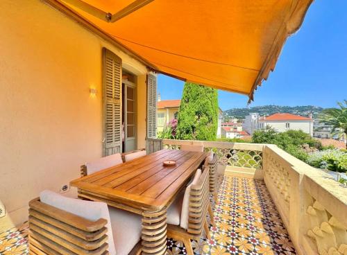 a wooden table and chairs on a balcony with an orange umbrella at Villa Leon - Centre Cannes - 4 chambres - Clim in Cannes