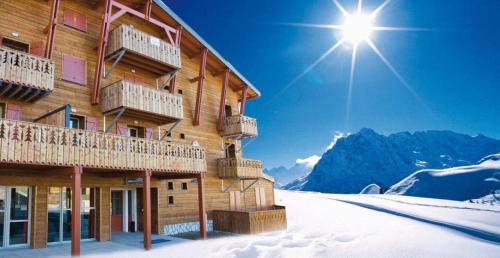 a ski lodge in the snow with the sun in the sky at Lagrange Vacances Les Chalets de l'Adet in Saint-Lary-Soulan