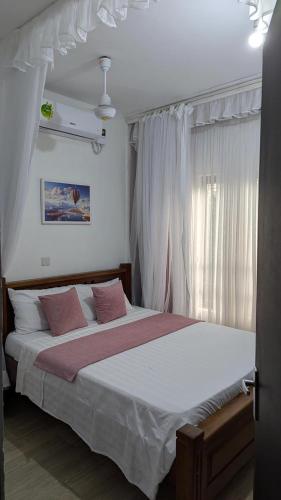 a bedroom with a large bed with white sheets and pink pillows at 1brm,2bdrm,3bdrm Palm Ridge Heavens Vipingo in Kilifi