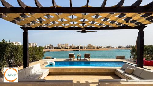 a swimming pool with a pergola next to the water at Heated Pool 4BR Villa, Lagoon Front, Ancient Sands - OllyStays in El Gouna
