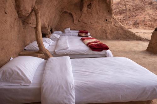 a group of four white beds in a cave at Wadi Rum Cave Camping in Wadi Rum