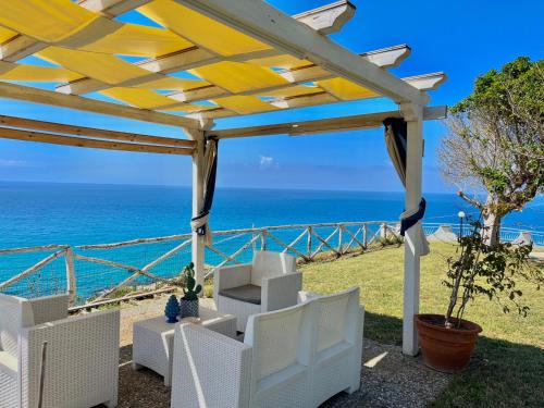 a wooden pergola with white chairs and the ocean at Residence Araba Fenice Tropea in Tropea