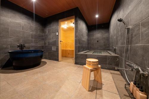 a bathroom with a black tub and a wooden stool at 玄 プライベートサウナ 大浴場付 光と木に包まれる和モダン一棟貸切 5寝室 最大26名 in Osaka