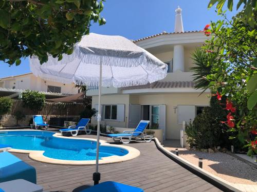 a house with a swimming pool with chairs and an umbrella at Vila Luisa Anabela Piscine et Jacuzzi in Albufeira