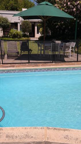 a swimming pool with chairs and a green umbrella at Hillcrest Cottage in Constantia