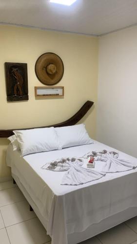 a bedroom with a bed with white sheets and a hat on the wall at Pousada Santa Adélia - Boipeba BA in Ilha de Boipeba