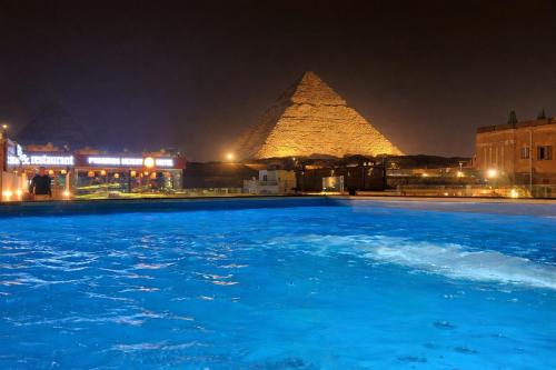 a swimming pool in front of the pyramids at night at Pyramids Height Luxury Wing in Cairo