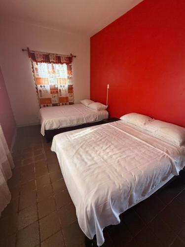 two beds in a room with a red wall at Casa Pelícanos playa de chachalacas in Ursulo Galván