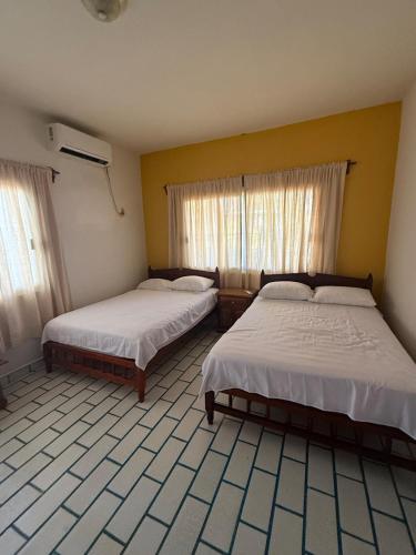 two beds in a room with yellow walls and windows at Casa Pelícanos playa de chachalacas in Ursulo Galván
