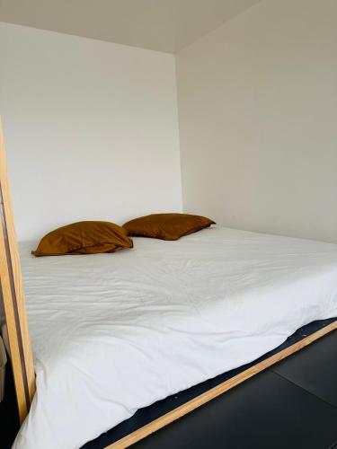 a bed with white sheets and brown pillows on it at Brõcean - Studio with sea view - in Loctudy