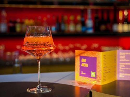 a glass of wine sitting on a table next to a book at ibis Styles Budapest Citywest in Budapest