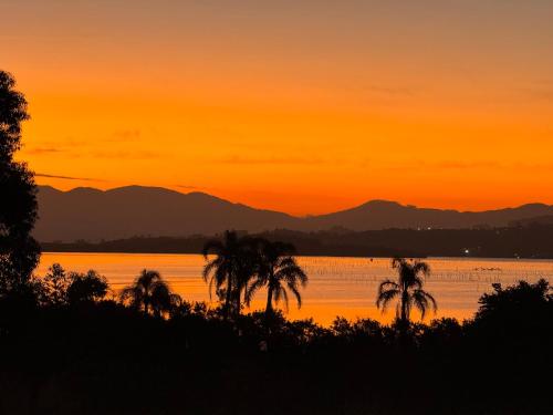 a sunset over the water with palm trees at Apartamento de frente para lagoa -Ap 101 in Laguna
