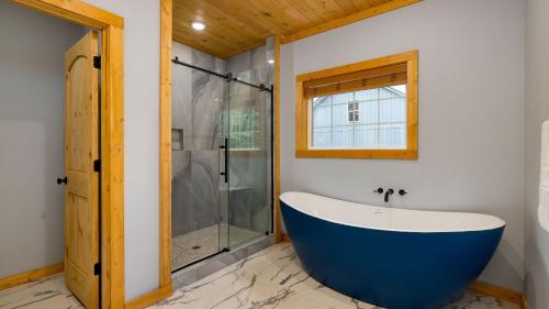 a bathroom with a blue tub and a glass shower at Cabin w Hot Tub Game Room Scenic Smoky Mountain Views Perfect by AvantStay in Gatlinburg