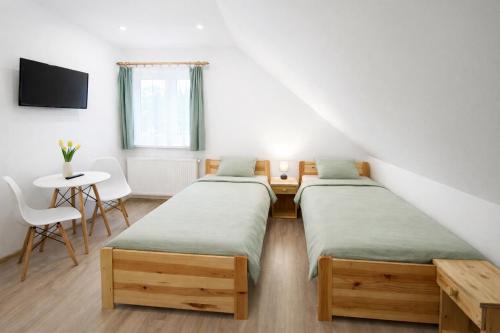two beds in a room with a table and a tv at Pokoje nad Dymnem in Koczała