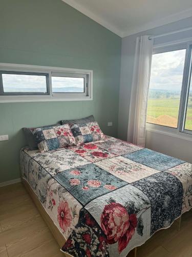a bedroom with a bed with a quilt and a window at Country Charm Cabins 2 Bedroom Tiny Home in Coolabunia