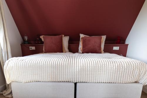 a large bed with red and white sheets and pillows at Slapen bij Bioduin in Koudekerke