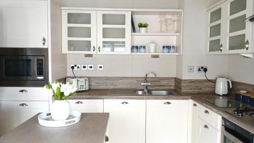 a kitchen with white cabinets and a sink at Luxury Lodge at Southview - perfect for couples with pond view and sun room in Skegness