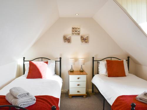 two beds in a attic room with white and orange pillows at Mont Stewart Cottage in Whiting Bay
