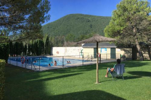 a person sitting in a chair under an umbrella next to a swimming pool at Apto Espert l PISCINA l Cine l Garaje l BBQ l Wifi in Biescas