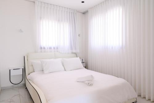 a white bedroom with a white bed with white curtains at וילה לה מר - וילה עם בריכה ו-3 סוויטות מדהימות עם נוף לים המלח in Neve Zohar