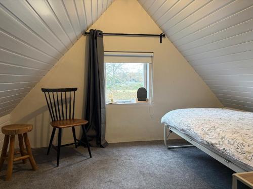 a bedroom with a bed and a chair and a window at Knus huisje met palletkachel in Tiendeveen