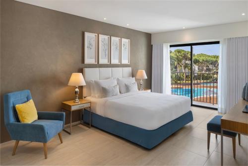 a bedroom with a large bed and a blue chair at Pine Cliffs Gardens in Albufeira